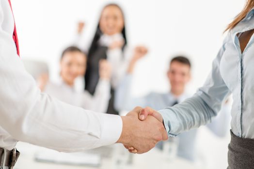 Close-up of a two business people shaking hands in front their successful business team in the office.