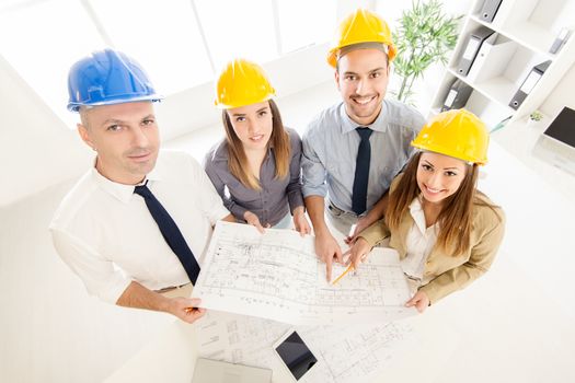 Top view of four successful architect checking the project. Looking at camera.