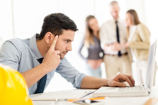 Young arabian male contractor sitting at desk in office and pensive looking at the laptop in front him.