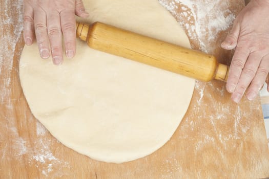 Hands baking dough with rolling pin on wooden table, depth of field