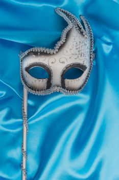 Colorful carnival mask on wavy blue satin fabric background. Top view with copy space.