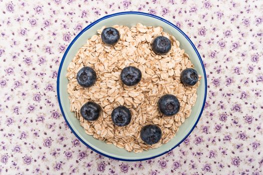 Oat flakes with blueberries in a bowl on cute fabric background. Top view with copy space.