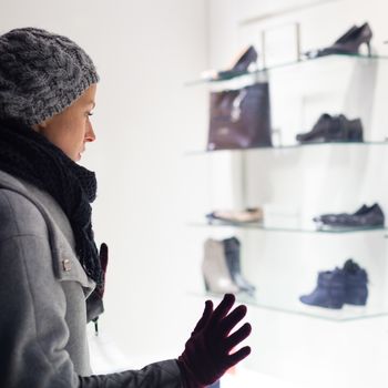 Casualy winter dressed lady window shopping in front of sinfully expensive boutique store dispaly window. Customer woman in shopping street, looking at window, outdoor.