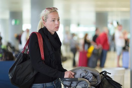 Casual blond young woman using her cell phone while queuing for flight check-in and baggage drop. Wireless network hotspot enabling people to access internet conection. Public transport.