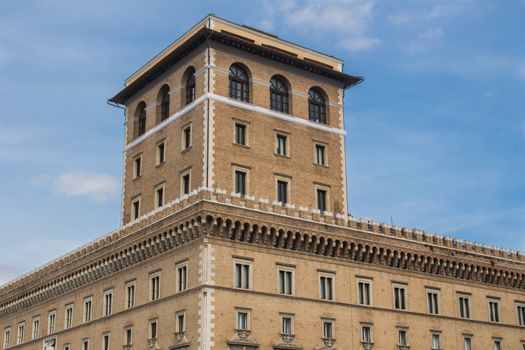 The outside of the Assicurazioni Generali building at Piazza Venezia in Rome. Facade made of bricks, unusual one tower. Blue sky with some clouds.