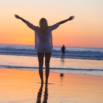 Silhouette of free woman enjoying freedom feeling happy at beach at sunset. Serene relaxing woman in pure happiness and elated enjoyment with arms raised outstretched up. 