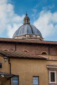 Typical orange colored building in Rome. Behind a dome of a church. Cloudy sky.