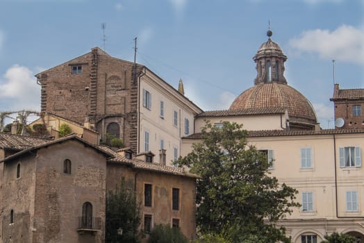 All shades of orange color of the facades of the roman houses. Dome of a church in the background. Blue sky with white clouds.