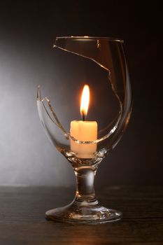 Lighting candle inside broken wineglass on dark background