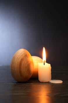 Two wooden eggs near candle on table against gray background