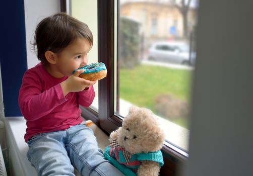 little girl and her bear toy eating  donuts