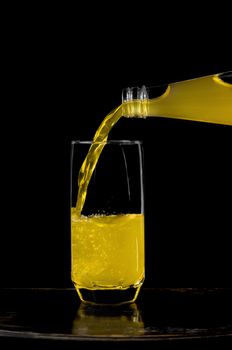 Lemonade pouring from bottle into a half full glass. Black background.