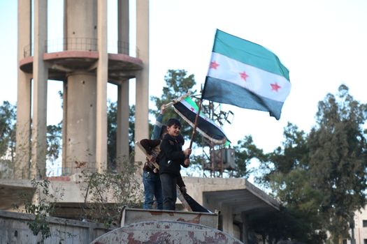 SYRIA, Saqba: Children hold a pre-Baath Syrian flag, that was adopted by the Syrian revolution during the uprising, on March 16, 2016 in Saqba, near Damascus, southern Syria, during a protest to mark the fifth anniversary of Syria's revolution. The conflict began with anti-regime protests in mid-March 2011 and spiralled into a bloody war after a harsh government crackdown on demonstrators. 