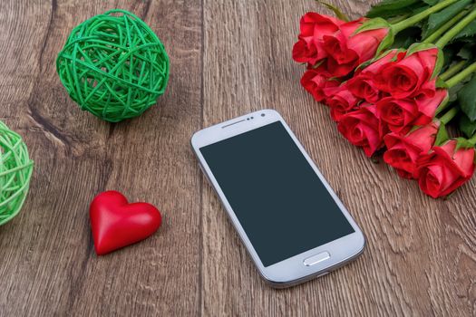 Mobile phone, red heart and red roses on a wooden background