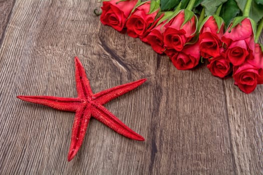 Red starfish and red roses on a wooden background