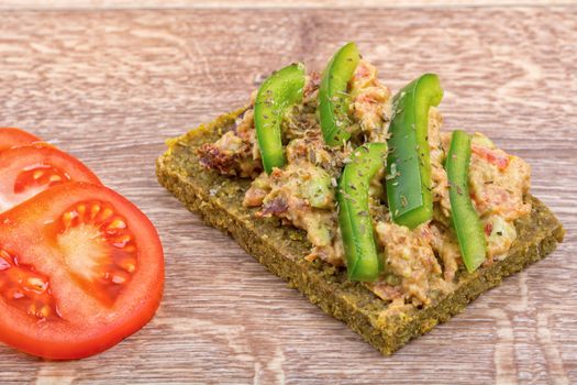 Raw bread with a spread decorated with green pepper and tomatoes