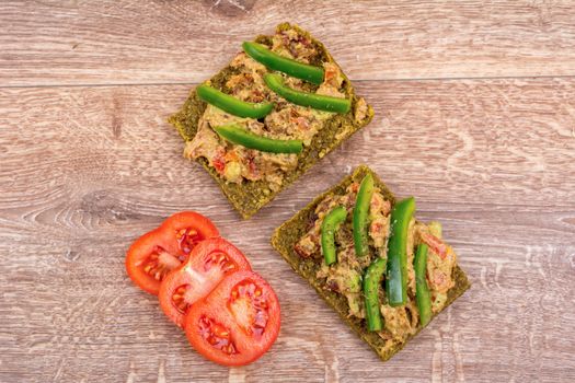Raw bread with a spread decorated with green pepper and tomatoes