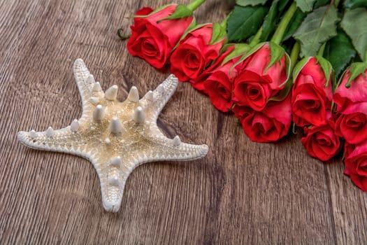 White starfish and red roses on a wooden background