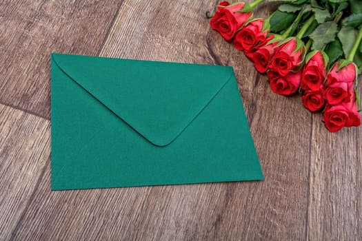 Green envelope and red roses on a wooden background
