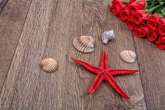 Red starfish and sea shells with red roses on a wooden background