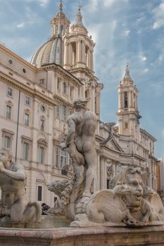 View from the back part on the statue at the fountain and Church Sant' Agnese in Agone. Cloudy sky with rays of sun.