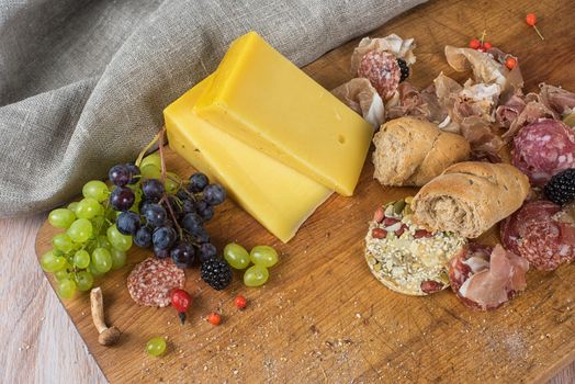 Fresh grapes, cheese bacon berries and salami on wooden table