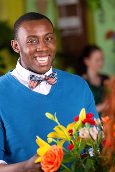 Laughing handsome young adult male in blue sweater purchasing a bouquet at a florist shop
