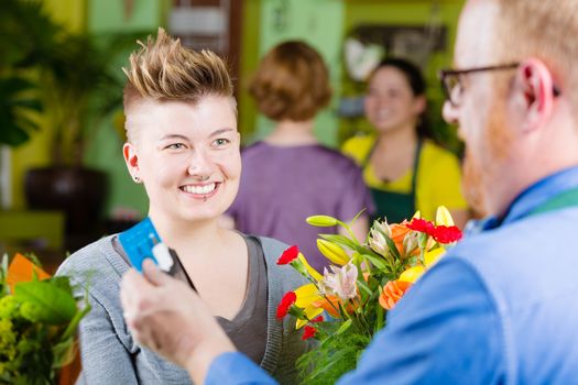 Young smiling customer watching floral shop clerk swipe credit card on tablet computer