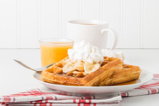 Plate of banana waffles with maple syrup and whipped cream.