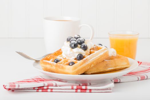 Plate of fresh waffles with blueberries, coffee and juice.