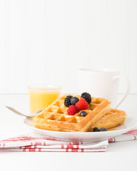 Plate of waffles with fresh fruit and maple syrup.