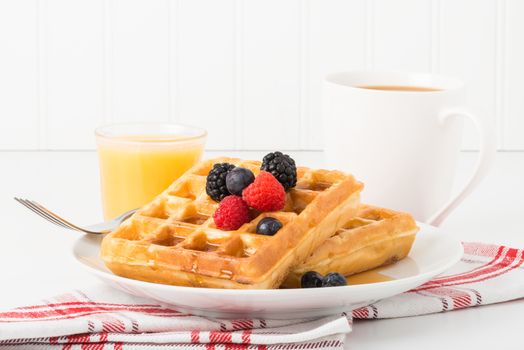 Stack of fresh waffles with maple syrup and fruit.