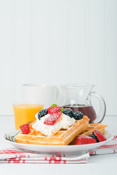 Plate of fresh waffles with berries, coffee and orange juice.