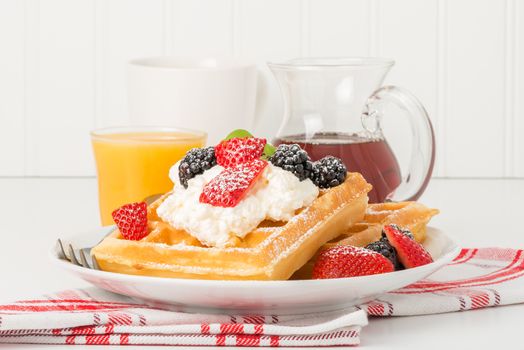 Plate of fresh waffles and berries with whipped cream and maple syrup.