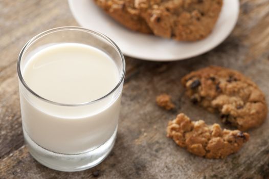 Full glass of fresh creamy milk with chocolate chip cookies on a wooden table for a tasty snack, high angle view