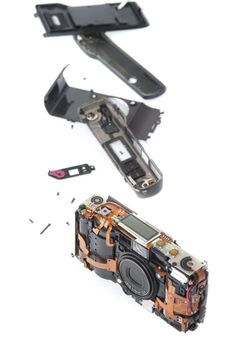 Single disassembled pocket camera with case pieces and exposed electronic parts over white background