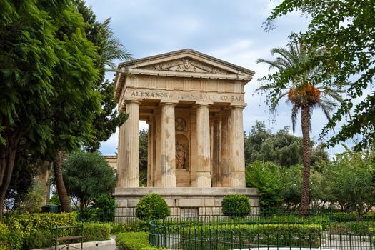 View of Lower Barrakka Gardens with historical monumental columns in Malta, with small trees around, on cloudy blue sky background.