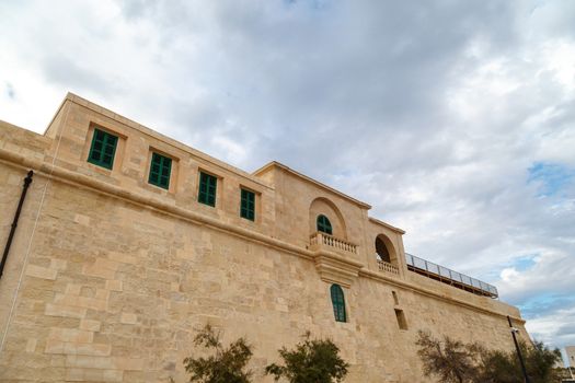 View of National War Museum in Valletta, Malta with high yellow stone walls, on cloudy sky background.