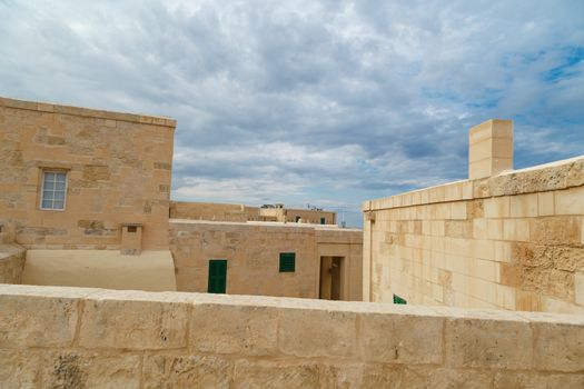 View of National War Museum in Valletta, Malta with high yellow stone walls, on cloudy sky background.