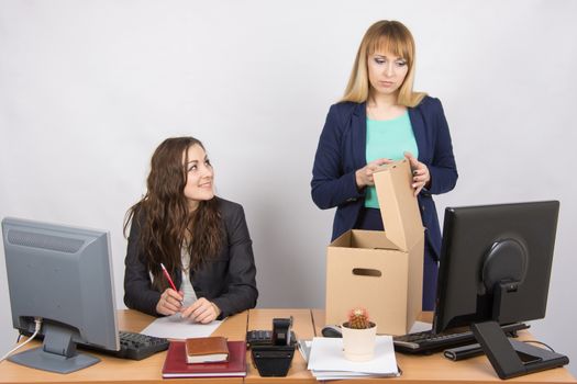 Office staff member with a smile, watching as a dismissed colleague collects things