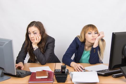 Two young office employee wearily sitting behind a desk