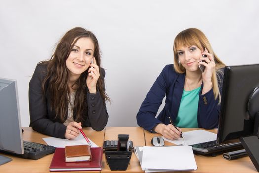 Two young office employee talking on mobile phones at his desk