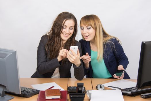 Two young office employee engaged in private affairs in a mobile phone at his desk