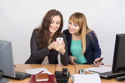 Two young office employee engaged in private affairs in a mobile phone at his desk