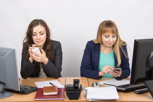 Two young office employee engaged in personal business in mobile phones at his desk