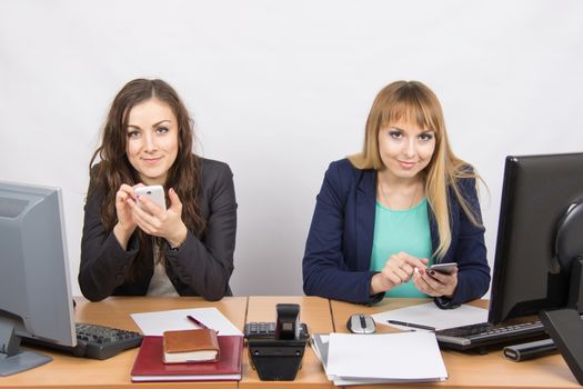 Two young office employee engaged in personal business in mobile phones at his desk