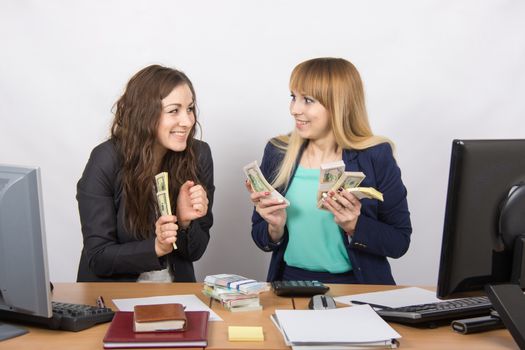 for office table two women collaborators happily hold hands in a pack with the money and express a strong admiration