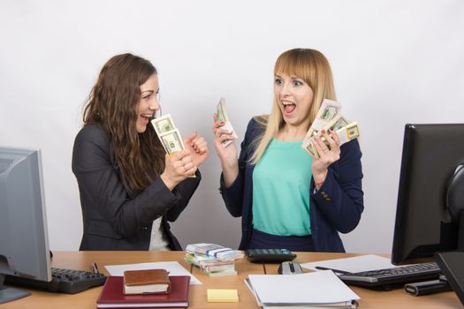 for office table two women collaborators happily hold hands in a pack with the money and express strong