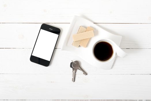 coffee cup with wafer,phone,key on white wood background