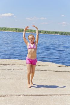 Dancing girl on the riverbank in pink swimsuit